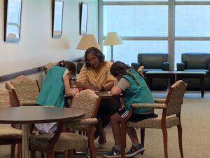 Two Girl Scouts writing with adult woman with tan and white sweater.